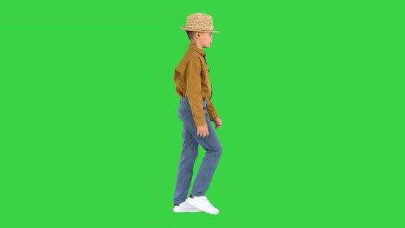 一个穿着衬衫的男孩一边走一边调整着他的草帽看着绿色屏幕上的摄像头ChromaKey