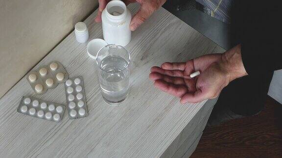 俯视图一位老人用一杯水把一剂药用胶囊药倒在手里处方治疗一个手里拿着药片的老人喝药