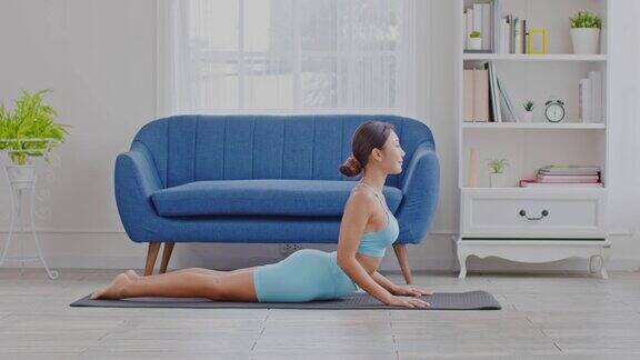 健康迷人的亚洲妇女在蓝色的穿着做瑜伽Cobra姿势在家里冥想舒适和放松冷静的健康年轻女子深呼吸和冥想与瑜伽在家里瑜伽概念