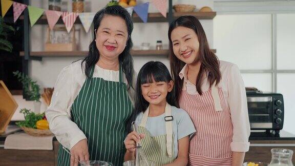 系着围裙的三代亚洲女性站在家里的厨房里微笑着看着镜头快乐的奶奶妈妈和小女儿在厨房里