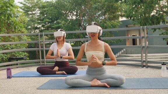 年轻的亚洲瑜伽老师和初学者女性戴着虚拟现实耳机运动上衣和紧身裤在城市公园户外练习瑜伽健康的生活方式和锻炼