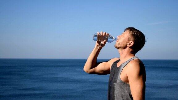 一名男子一边喝水一边把塑料瓶里的水倒在海里让自己在锻炼后神清气爽