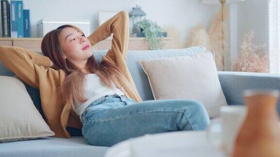 放松的年轻亚洲妇女享受休息在舒适的沙发在家里平静迷人的女孩放松和呼吸新鲜的空气在家里