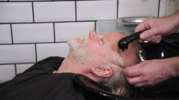 男士沙龙一名男理发师在理发店的水槽里为一位老人在专业的椅子上洗头