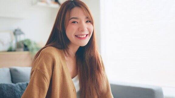 自信的微笑年轻的成年亚洲女人坐在家里看着相机快乐的美丽的女士漂亮的脸牙齿微笑独自在室内摆姿势