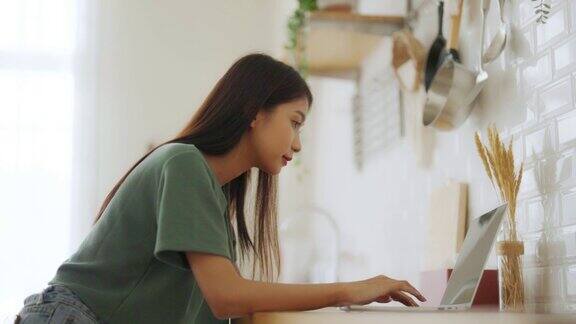 微笑的亚洲年轻女性在家庭办公室的笔记本电脑上工作年轻亚洲学生使用电脑远程学习虚拟培训在线学习观看在线教育网络研讨会