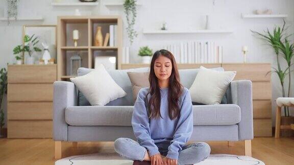 快乐的年轻亚洲女性在家里练习瑜伽和冥想坐在客厅的地板上以莲花的姿势闭上眼睛放松正念冥想和幸福概念