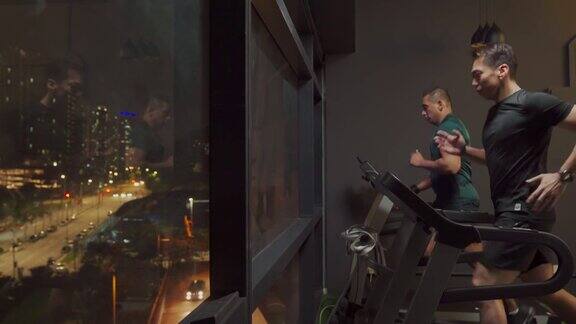 侧视宽镜头身体强壮的男人一起在健身房跑步机在晚上面对城市的街灯