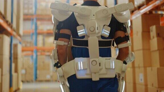 高科技未来仓库:工人穿着先进的全身动力外骨骼与沉重的纸板箱行走Exosuit增强了人类的力量特写慢动作弧光灯
