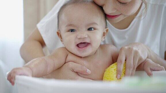 亚洲妈妈在婴儿浴缸里给婴儿洗澡婴儿笑着玩家庭关系概念