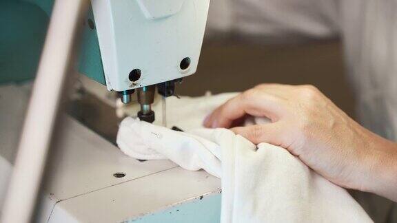 在复古工作室工作的专业女裁缝女裁缝用时髦的指甲用缝纫针和白线缝制白色织物创造完美的接缝车间缝纫过程的细节女裁缝用复古缝纫机工作