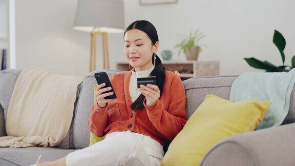 快乐的女人信用卡和电话在沙发上网上购物电子商务和金融科技轻松支付在中国的亚洲人用手机输入银行信息在家里进行折扣或金融交易