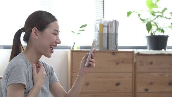 幸福的亚洲女性拿着信用卡在家里的卧室里用智能手机在线购物