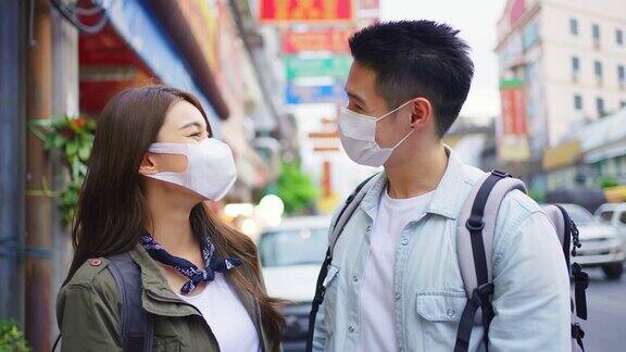 亚洲夫妇戴着面具在城市旅行度蜜月新婚男女背包客在疫情期间开心地一起享受假期然后看着镜头
