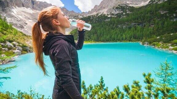 女人在山湖边从一个可重复使用的水瓶补水