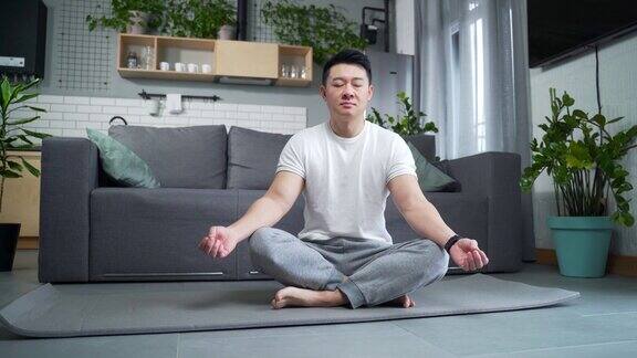 亚洲运动男子练习瑜伽坐在垫子上的莲花位置在家里的客厅冷静的男性在室内冥想和放松
