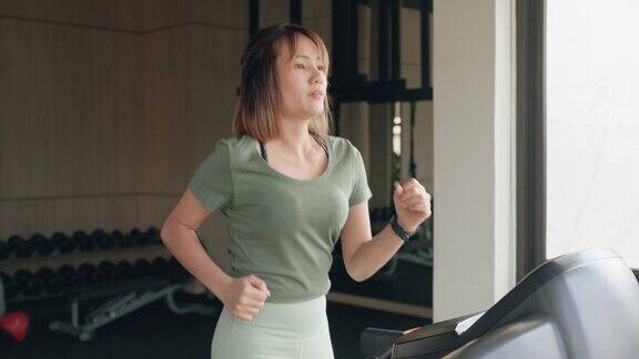年轻的亚洲体育女运动员在跑步机上跑步在现代健身房积极训练体育人士锻炼