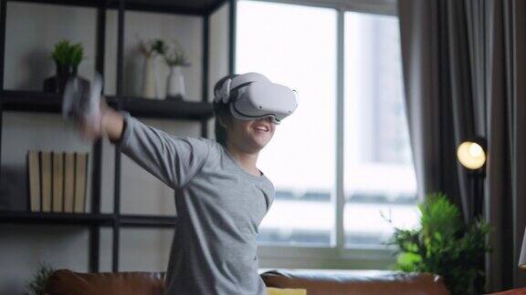 在隔离期亚洲儿童男孩戴着VR或虚拟现实眼镜站在家中客厅的电视机前玩电子游戏