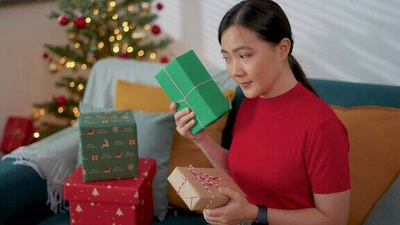 圣诞节那天一个亚洲女人坐在客厅里开心地笑着摇着礼盒