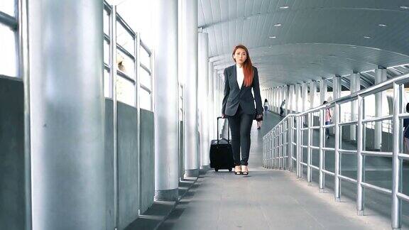 背影的慢动作镜头迷人的亚洲商务女性拖着一个轮式行李箱在机场出差