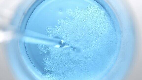 滴管将油注入烧杯中的蓝色液体中产生气泡