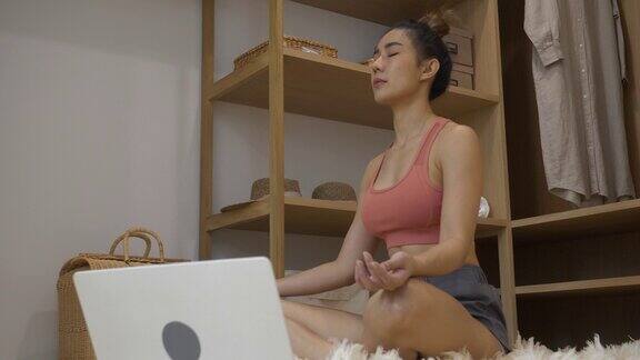 运动女性在家健身锻炼锻炼在客厅看笔记本电脑在线教练年轻女子在地板上使用笔记本电脑运动服装手臂伸展身体重量训练健康的生活方式理念