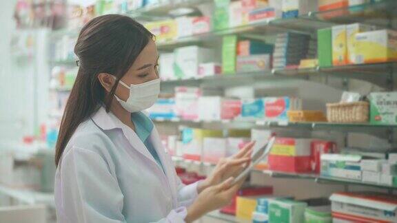 一位亚洲女性药剂师穿着实验服和防护口罩在一家现代药店使用药片分析医疗数据