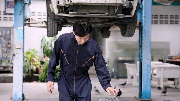 亚洲男性汽车修理工正在滚动汽车轮胎由熟练的机械师将4个轮胎全部换好后再把汽车停放在车库里等待修理以便重新使用