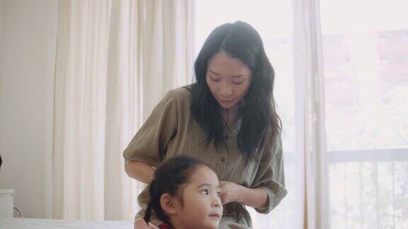 亚洲母亲编织头发她的女儿准备上学