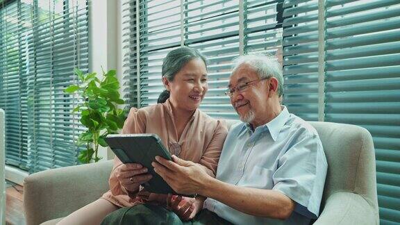 退休的亚洲老人思考着过去的生活而老奶奶带着平板电脑和他一起看相册的肖像