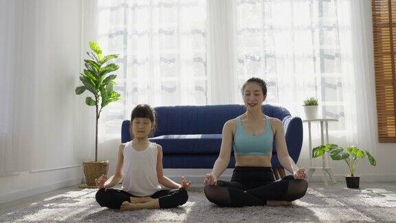 画像年轻的亚洲母亲女儿准备伸展后在瑜伽冥想妈妈和小女儿在家里的瑜伽垫上练习瑜伽一起生活母亲节理念