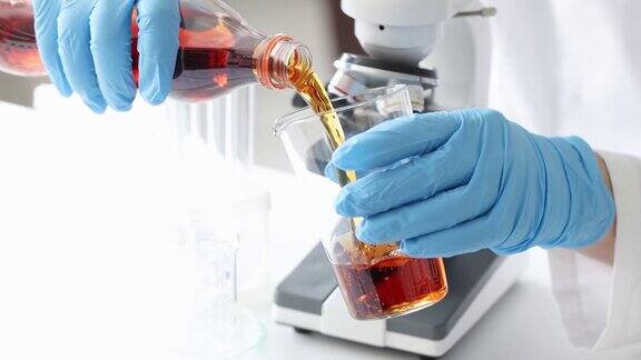 戴着手套的科学家在实验室里把棕色液体从瓶子倒进玻璃烧杯里这是一部4k慢动作电影