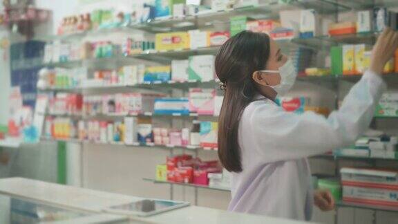 一位亚洲女性药剂师穿着实验服和防护口罩在一家现代药店使用药片分析医疗数据