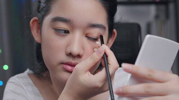 年轻的亚洲影响者女孩在视频中示范如何用美容化妆品化妆她在家里的客厅里用摄像机录制在线辅导课社交媒体和直播病毒概念