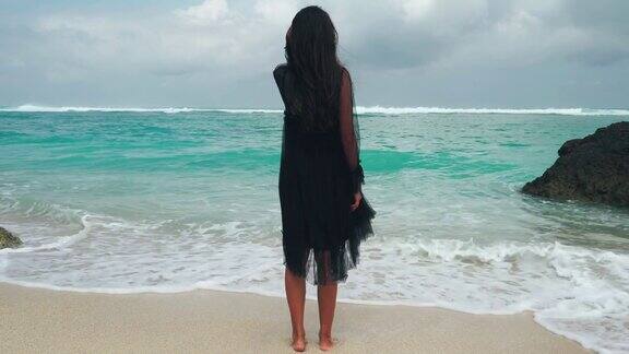 以汹涌的大海为背景穿着黑色连衣裙的女孩