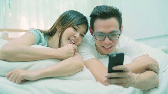 一对幸福的情侣在床上玩着智能手机