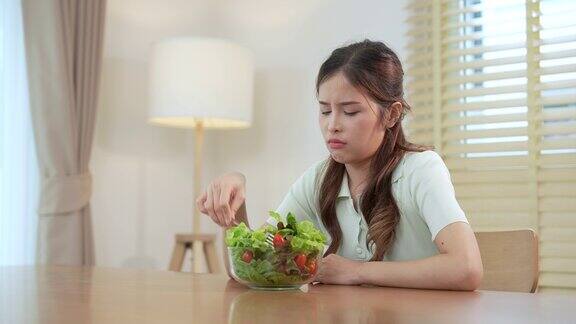 不快乐的女人无聊地看着面前的一碗有机蔬菜沙拉因为她不喜欢吃蔬菜