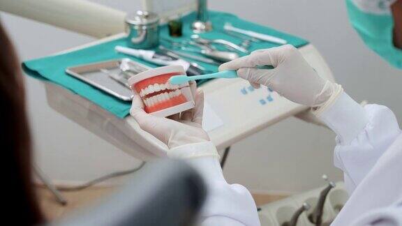 牙科医生向坐在牙科椅上的病人展示如何使用口腔和牙齿模型正确刷牙