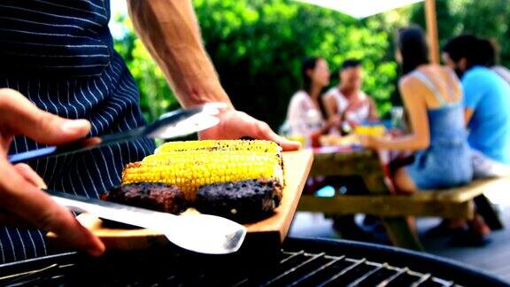 一名男子正在为户外烧烤聚会准备烤肉和玉米