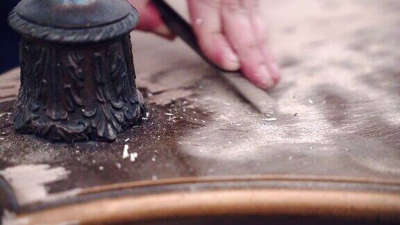 用金属凿去除木板表面的旧漆木匠用青铜腿打磨古色古香的桌子表面技工在车间修复木桌