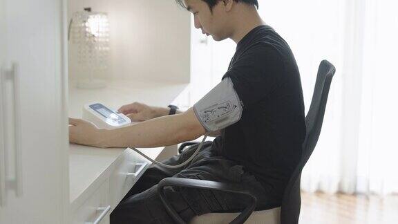 年轻的亚洲男子坐在办公桌前手臂上戴着血压计测量结束后取下
