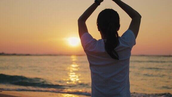 日落时分在海滩上做树瑜伽姿势的剪影女孩
