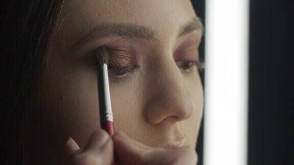 化妆的步骤化妆师用化妆刷在女孩的眼睛上涂上深色眼影