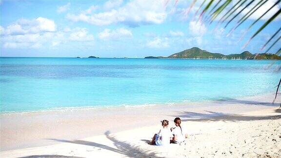 两个小女孩在沙滩上快乐的孩子们坐在热带海滩上的棕榈树下