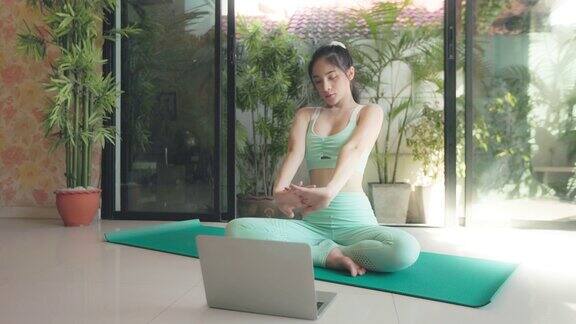 年轻的亚洲妇女在家里玩瑜伽在线健康或健康的生活方式