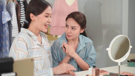 两个年轻漂亮的亚洲女孩做视频录制现场蒸销售化妆品在线亚洲女性化妆师在服装化妆品店向网上顾客推荐粉底美女直播