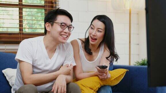 年轻的亚洲夫妇看电视与幸福在家庭客厅的沙发背景人和家庭娱乐