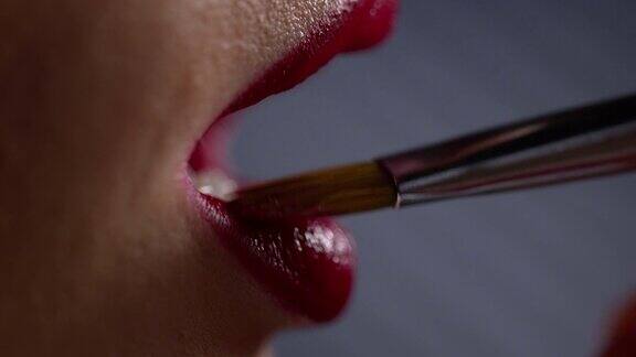 用化妆刷在女人的嘴唇上涂红色唇膏