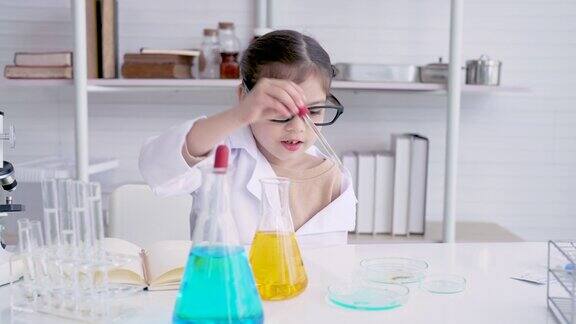 4K亚洲女孩个子小坐在科学教室里在科学课上学习在实践课上他从烧瓶里挤水挤到烧杯里作为老师分配的分数他喜欢实验