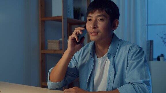 年轻的亚洲人打电话坐在工作桌旁客厅在家里的晚上